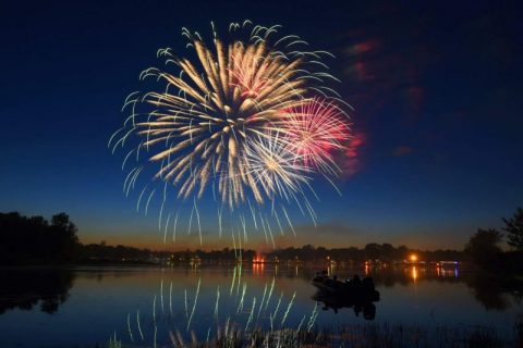 Firework display against a dark blue evening sky with reflection over a lake
